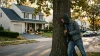 Homme en hoodie caché derrière arbre observant maison