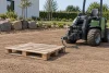 Palette posée à plat sur un terrain nivelé près d’un engin de jardinage arrêté et inoccupé.