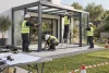 Professionnels équipés assemblant une structure modulaire de véranda générique sur une dalle sécurisée.