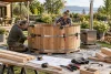 Deux adultes assemblant prudemment une cuve ronde en bois dans un jardin.